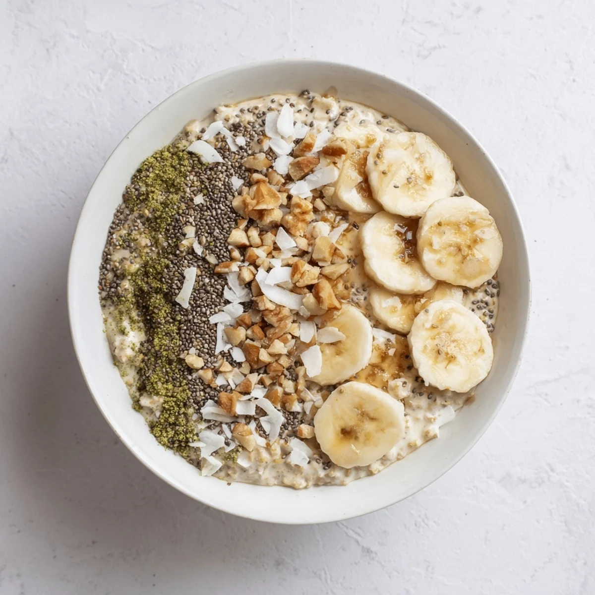 Creamy High-Protein Eggnog Matcha Overnight Oats with banana slices and toasted coconut, perfect breakfast.