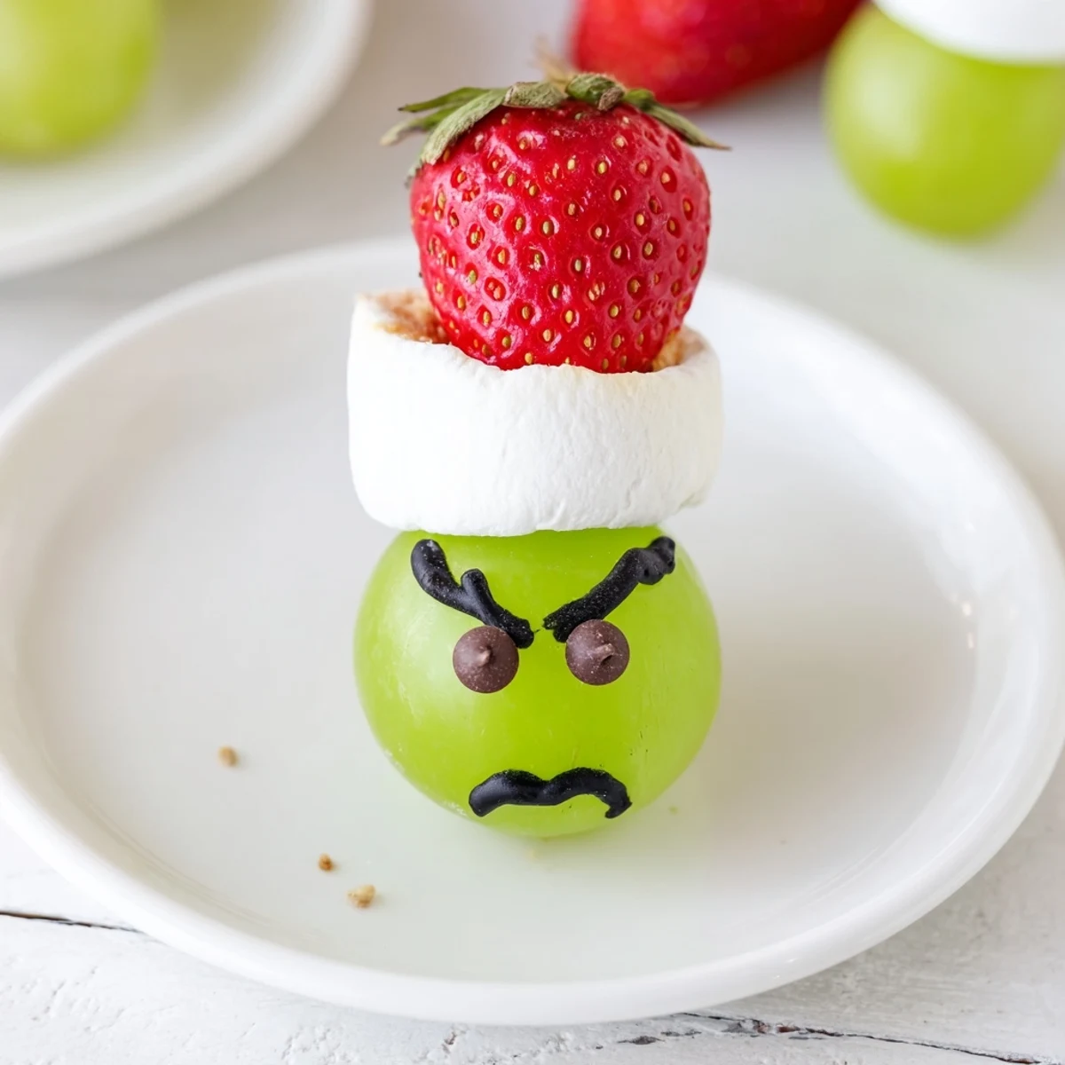Kid-friendly Grinch Snack with green grapes, marshmallows, and strawberry hats, perfect for Christmas.