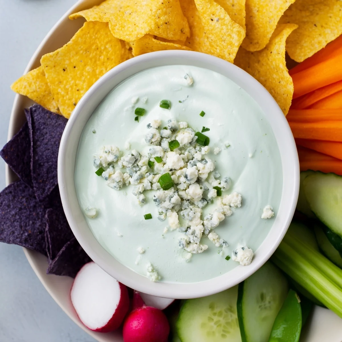 This creamy Frozen Pond Blue Dip is surrounded by a vibrant array of crunchy snacks and vegetables.