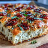 Fluffy focaccia bread topped with vibrant rosemary, thyme, chives, and juicy cherry tomatoes, ideal for sharing at gatherings.  