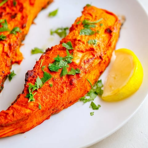 Golden-brown Indian tikka salmon glistens, ready to be served with fresh cilantro and lemon.
