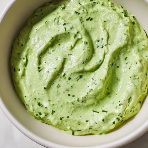 A close-up of creamy Green Goddess Salad Dip garnished with fresh chopped herbs, served in a rustic bowl next to colorful veggie sticks and tortilla chips.