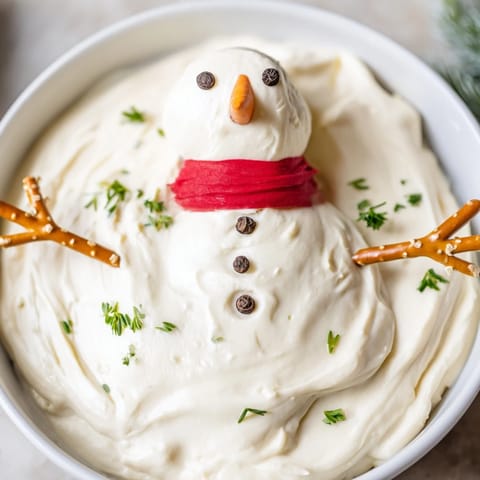 Festive Melted Snowman Dip, a holiday appetizer featuring a creamy dip, carrot noses, and pretzel arms.