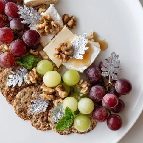 This Sparkling Grape and Silver Cracker Platter showcases a mouthwatering array of grapes, cheeses, and silver-dusted crackers for elegant entertaining.