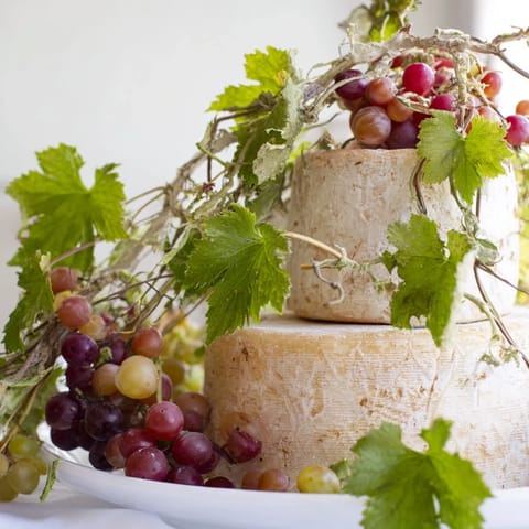 The Rustic Vineyard arrangement showcases wheels of cheese adorned with grapevines for serving.