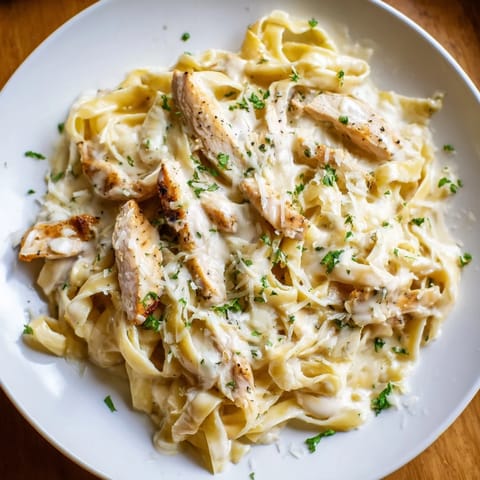 A close-up of skillet Chicken Alfredo with glossy cream sauce clinging to pasta and tender chicken, served hot with a side salad and crusty bread.  