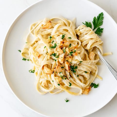 Al dente fettuccine coated in velvety roasted garlic cream sauce, steaming in a rustic kitchen setting.  