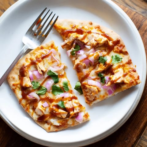 A close-up of BBQ Chicken Flatbread, featuring gooey cheese, tangy sauce, and fresh cilantro garnish.