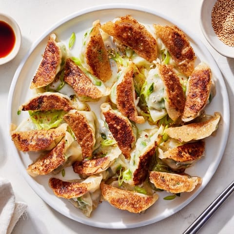 Crispy smashed gyozas arranged on a white plate with green onions and a small bowl of soy-vinegar dipping sauce.