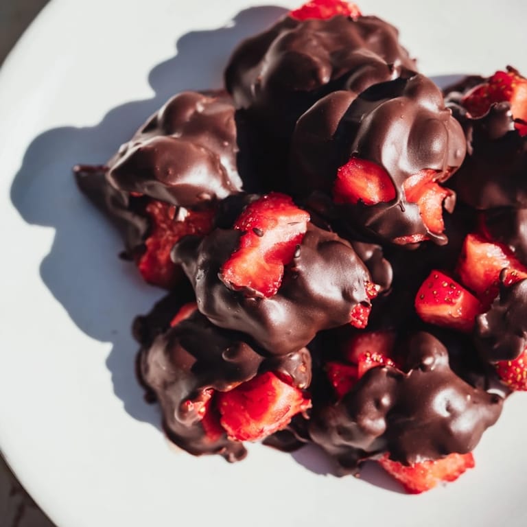 Melted chocolate enrobes vibrant Strawberry Yogurt Clusters, a visually stunning frozen dessert option.